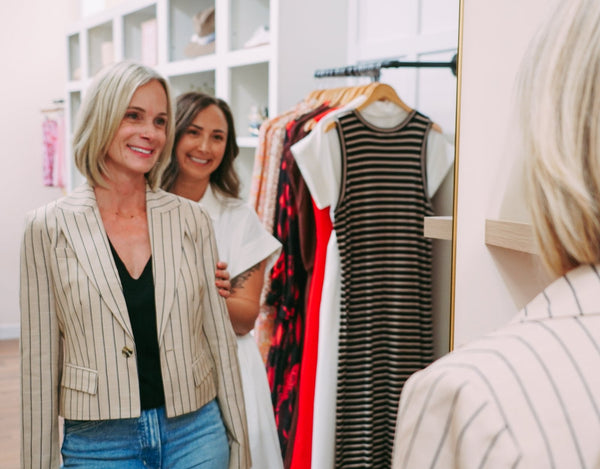 A smiling client admires her new striped blazer in the mirror as Jenna smiles behind her at Style Curated